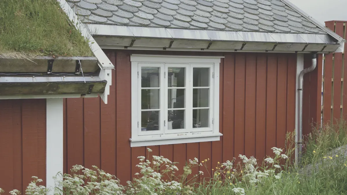 Rödmålad svensk sommarstuga med torvtak och vita fönsterfoder en sommardag
