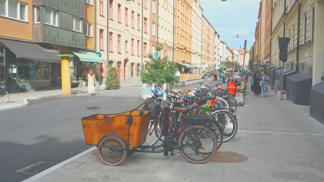 Trehjulig lådcykel med stor trälåda parkerad vid ett cykelställ på en stadsgata